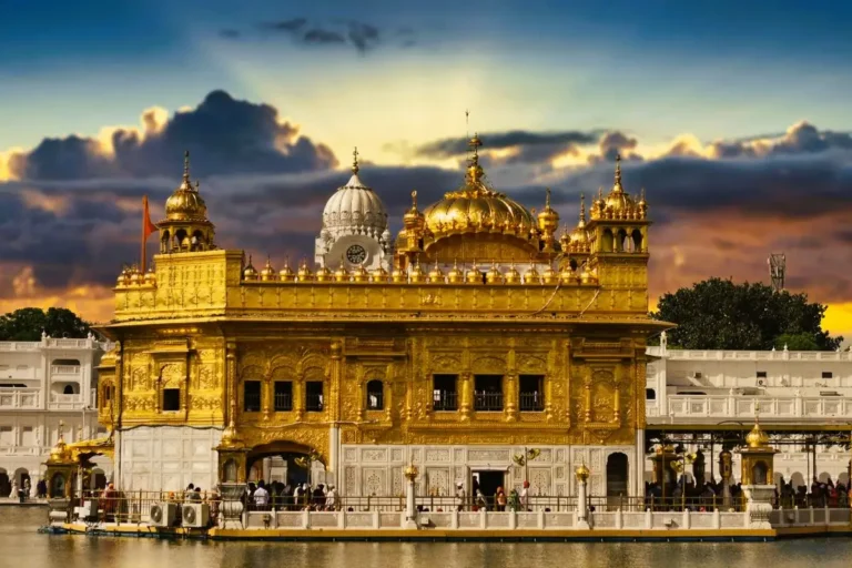 The Golden Temple in Amritsar glowing under a dramatic sunset sky with water in the foreground
