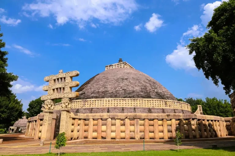 The ancient stone dome structure of the Sanchi Stupa featuring an ornate carved torana gateway under a blue sky