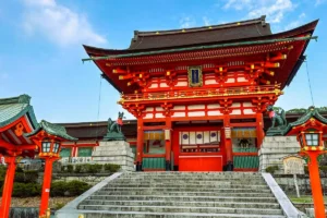 The grand vermilion Romon Gate and stone entrance steps at Fushimi Inari shrine in Kyoto, guarded by stone fox statues.