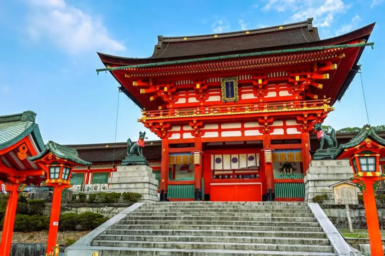 The grand vermilion Romon Gate and stone entrance steps at Fushimi Inari shrine in Kyoto, guarded by stone fox statues.