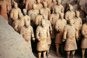 Rows of life-sized clay warriors with intricately detailed armor standing in an excavated earthen trench at the Terracotta Army Museum