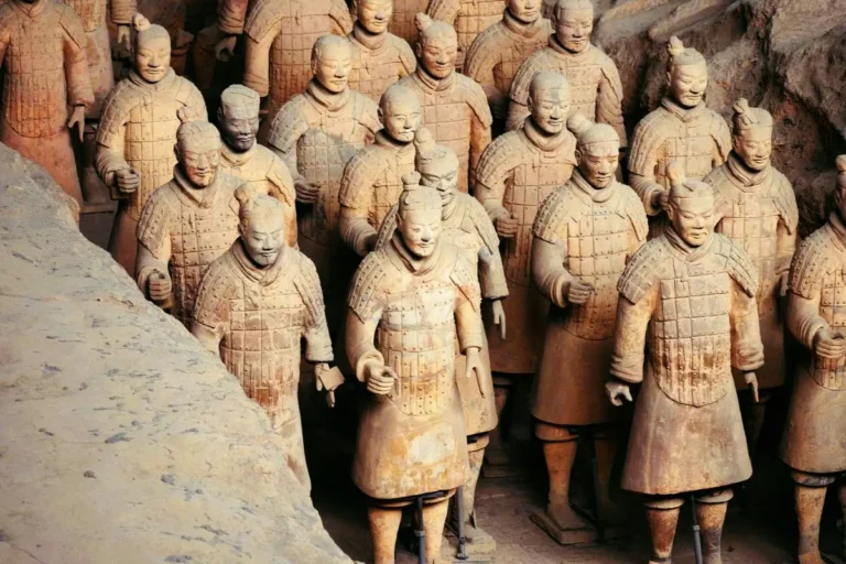 Rows of life-sized clay warriors with intricately detailed armor standing in an excavated earthen trench at the Terracotta Army Museum